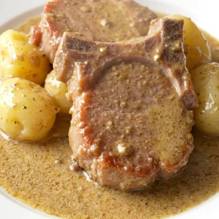 A close-up of tender, slow-cooked pork chops covered in a rich, creamy mushroom gravy with soft baby potatoes.