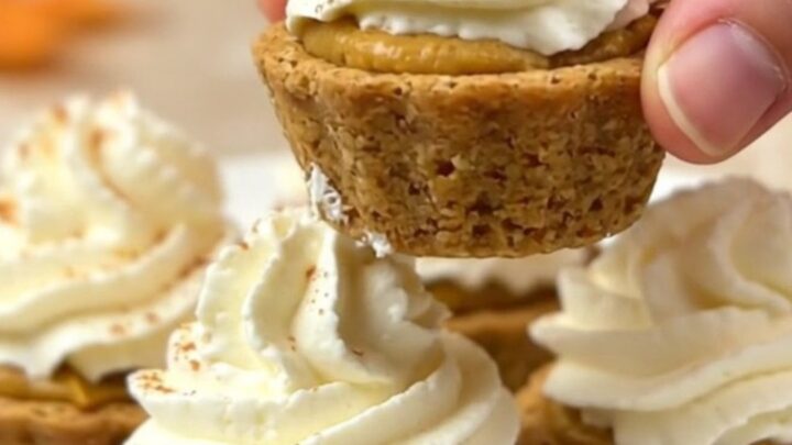A top-down view of twelve mini pumpkin pie bites arranged on a parchment-lined baking sheet on a beige countertop.