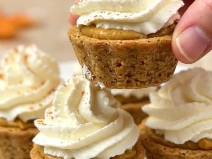 A top-down view of twelve mini pumpkin pie bites arranged on a parchment-lined baking sheet on a beige countertop.