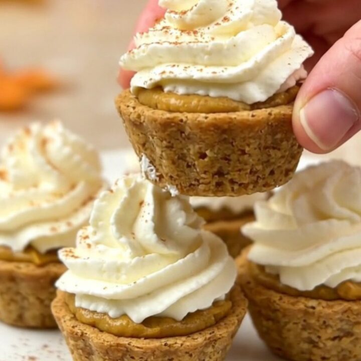 A top-down view of twelve mini pumpkin pie bites arranged on a parchment-lined baking sheet on a beige countertop.