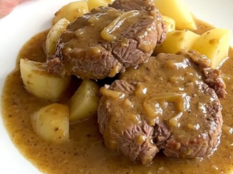 Slow cooker smothered round steak with tender potatoes in a rich onion gravy in a white bowl.