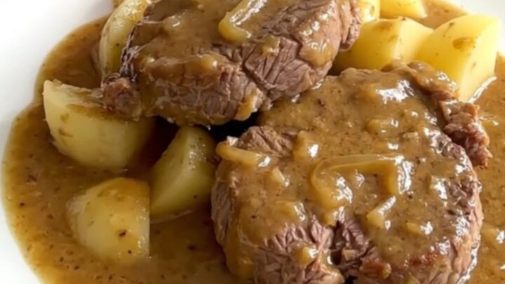 Slow cooker smothered round steak with tender potatoes in a rich onion gravy in a white bowl.
