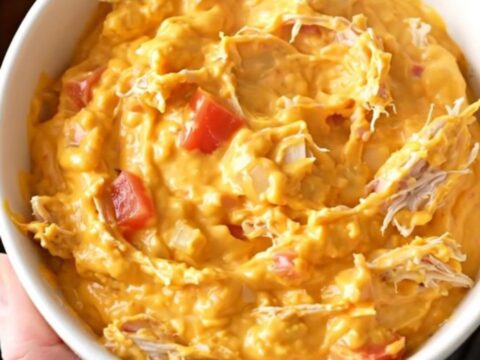 A close-up view of creamy chicken nacho dip in a slow cooker, showing shredded chicken and melted cheese.
