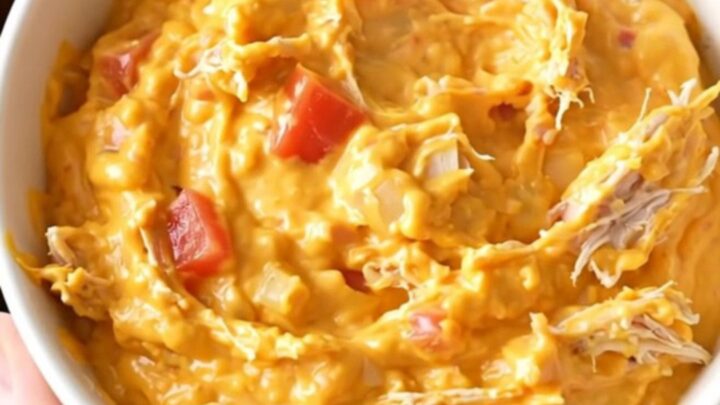 A close-up view of creamy chicken nacho dip in a slow cooker, showing shredded chicken and melted cheese.