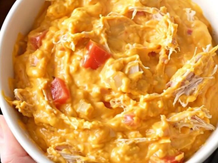 A close-up view of creamy chicken nacho dip in a slow cooker, showing shredded chicken and melted cheese.