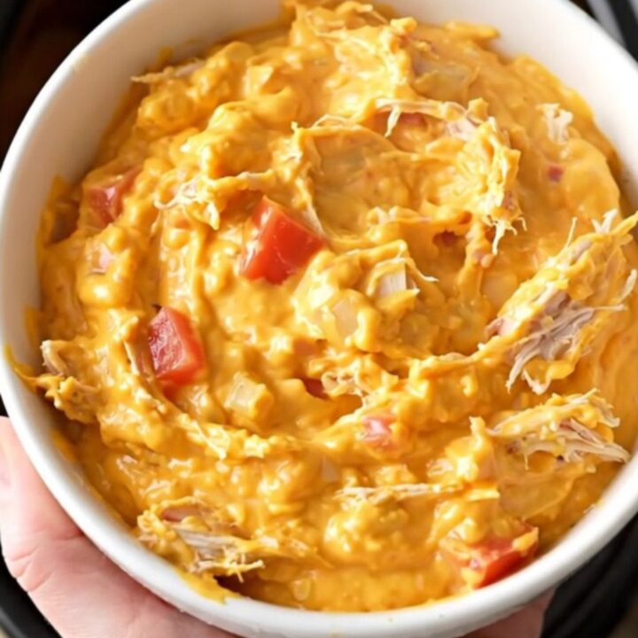 A close-up view of creamy chicken nacho dip in a slow cooker, showing shredded chicken and melted cheese.