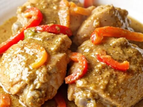 A high-angle shot of raw chicken thighs in a slow cooker topped with colorful pepper strips and jerk seasoning.