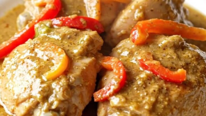 A high-angle shot of raw chicken thighs in a slow cooker topped with colorful pepper strips and jerk seasoning.
