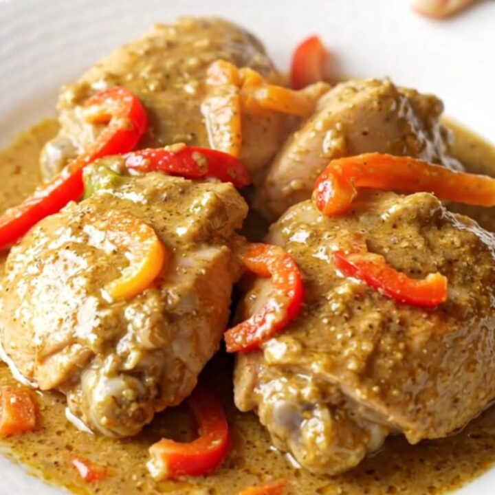 A high-angle shot of raw chicken thighs in a slow cooker topped with colorful pepper strips and jerk seasoning.