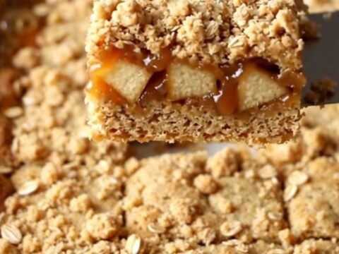 A top-down view of freshly baked caramel apple crumble bars in a ceramic dish, showing golden oats and caramel.