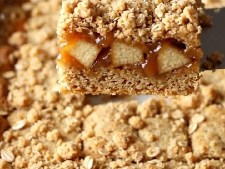 A top-down view of freshly baked caramel apple crumble bars in a ceramic dish, showing golden oats and caramel.