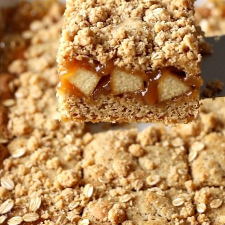 A top-down view of freshly baked caramel apple crumble bars in a ceramic dish, showing golden oats and caramel.