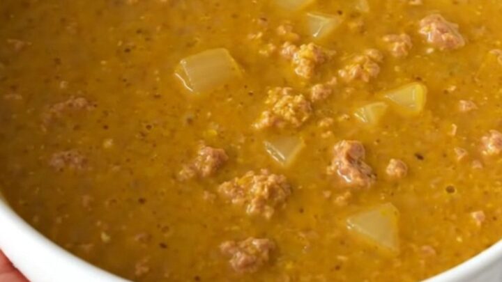 A warm, inviting bowl of creamy pumpkin sausage soup with visible sausage crumbles and herbs.