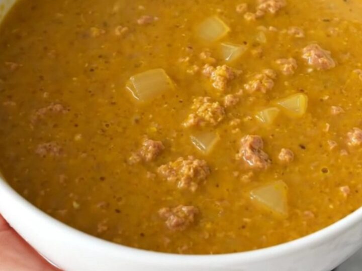 A warm, inviting bowl of creamy pumpkin sausage soup with visible sausage crumbles and herbs.
