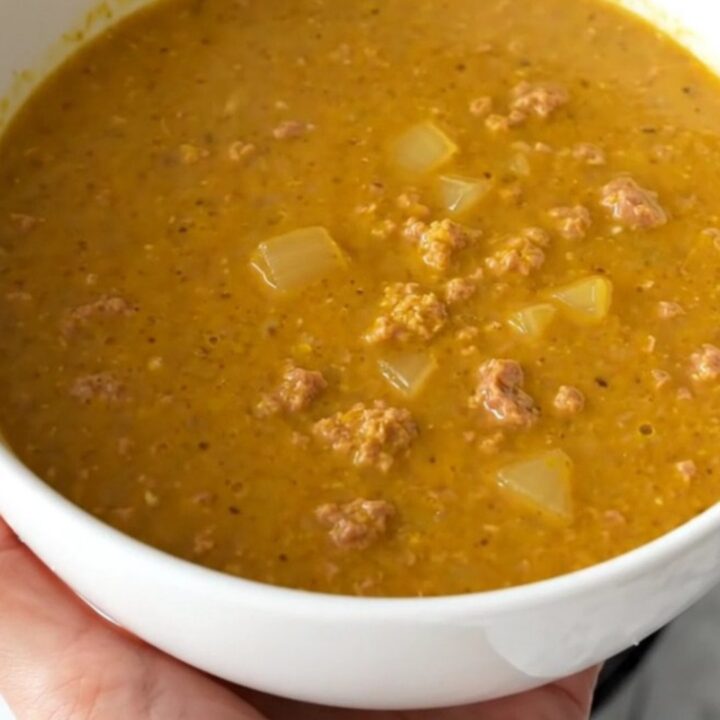 A warm, inviting bowl of creamy pumpkin sausage soup with visible sausage crumbles and herbs.