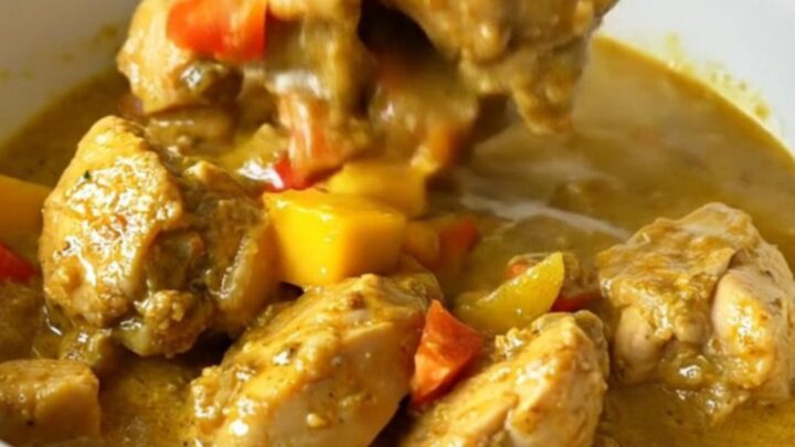 A top-down view of a slow cooker filled with chicken, mango, and red bell pepper in a golden curry sauce.