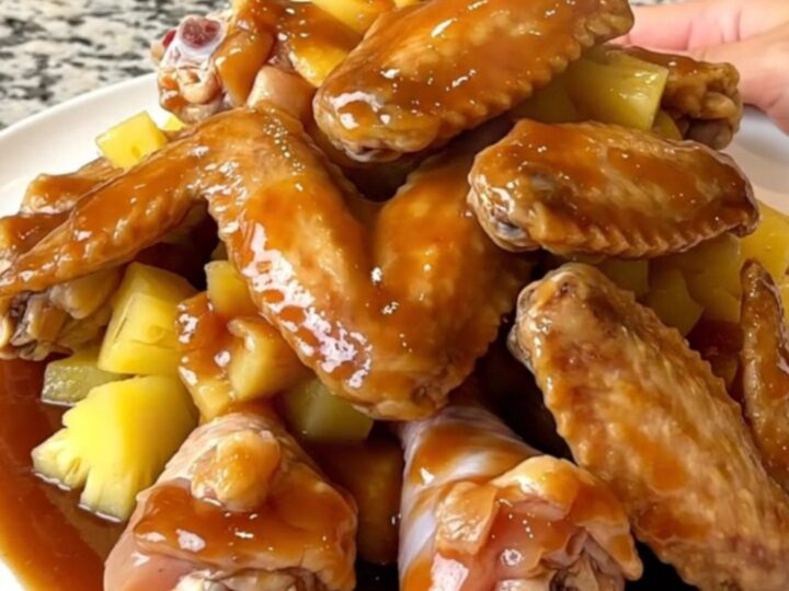 Slow cooked chicken wings in a rich, dark huli huli sauce with pineapple chunks in a black slow cooker insert.