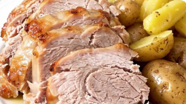A whole, golden-brown pork loin roast sitting in a slow cooker surrounded by tender baby potatoes.