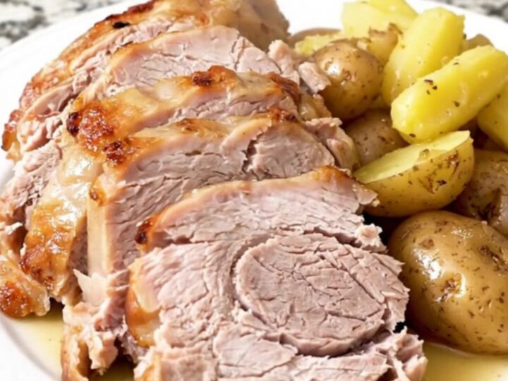 A whole, golden-brown pork loin roast sitting in a slow cooker surrounded by tender baby potatoes.