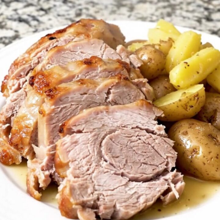 A whole, golden-brown pork loin roast sitting in a slow cooker surrounded by tender baby potatoes.