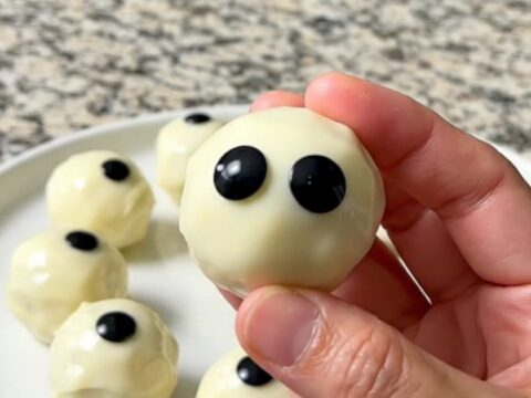 A tray of finished dark cookie truffle eyeballs coated in white chocolate with candy eyes.