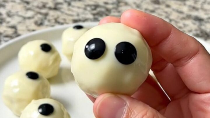 A tray of finished dark cookie truffle eyeballs coated in white chocolate with candy eyes.