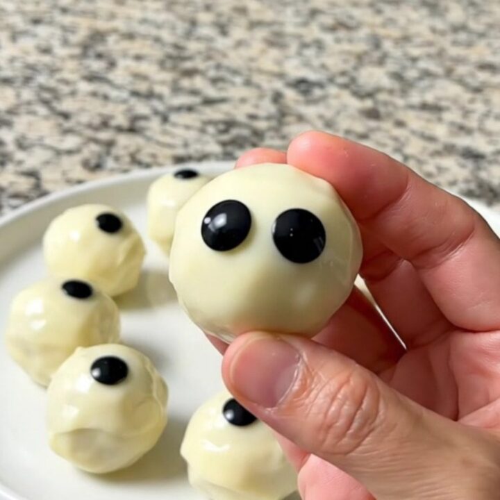 A tray of finished dark cookie truffle eyeballs coated in white chocolate with candy eyes.