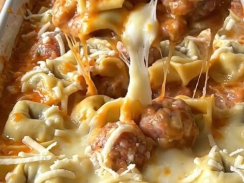 A top-down view of a rectangular baking dish filled with cheese tortellini, meatballs, and creamy sauce