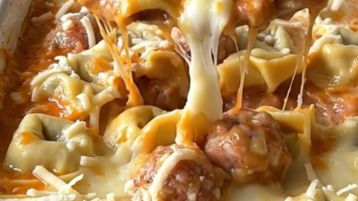 A top-down view of a rectangular baking dish filled with cheese tortellini, meatballs, and creamy sauce