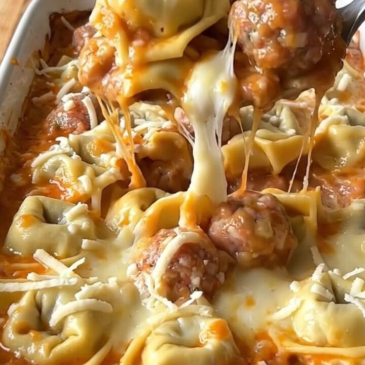 A top-down view of a rectangular baking dish filled with cheese tortellini, meatballs, and creamy sauce