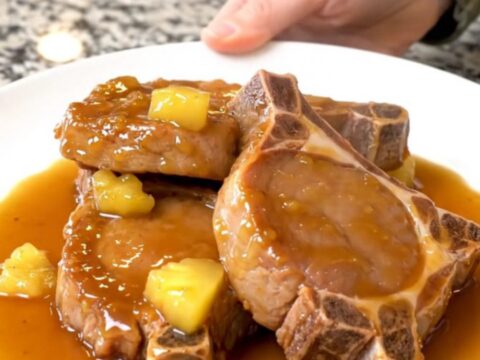 A plate of tender, braised Hawaiian pork chops topped with pineapple chunks and a glossy, sweet sauce.
