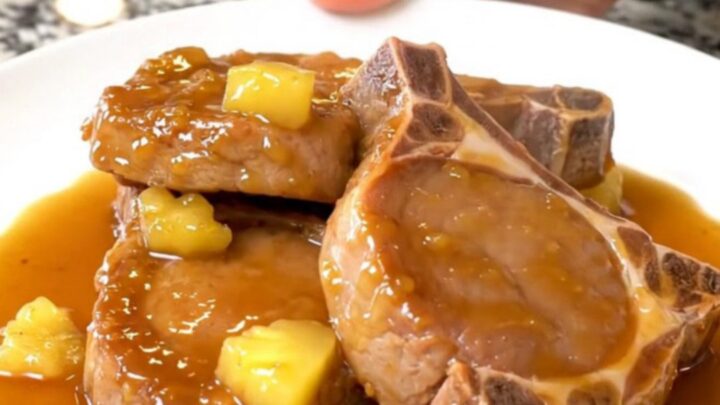 A plate of tender, braised Hawaiian pork chops topped with pineapple chunks and a glossy, sweet sauce.