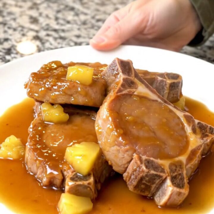 A plate of tender, braised Hawaiian pork chops topped with pineapple chunks and a glossy, sweet sauce.