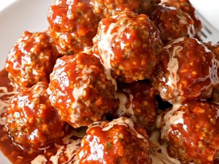 A slow cooker filled with turkey meatballs coated in a glossy, creamy pepper jelly sauce.