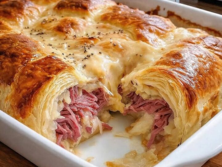 A golden-brown Reuben Crescent Bake in a ceramic dish, showing flaky pastry layers.