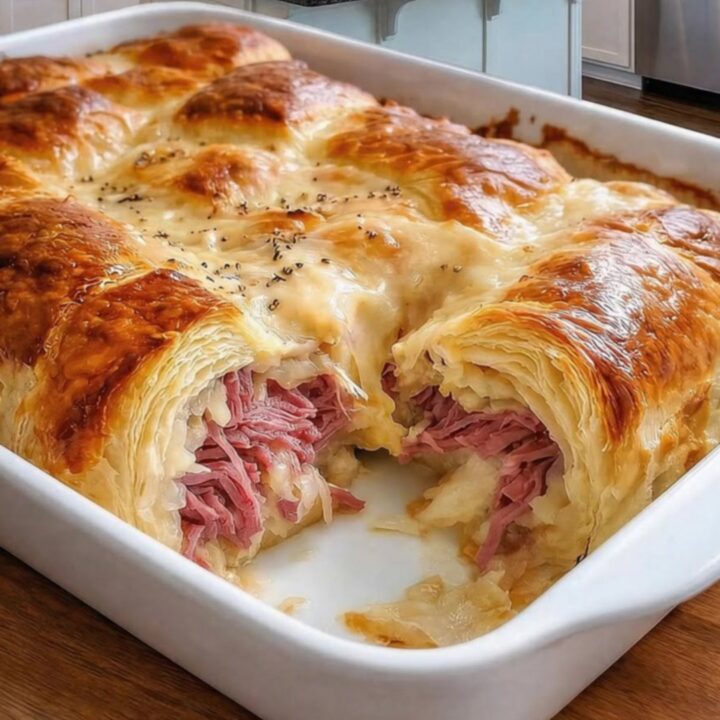 A golden-brown Reuben Crescent Bake in a ceramic dish, showing flaky pastry layers.