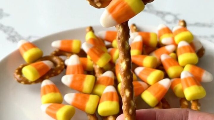 A plate of candy corn pretzel rods featuring a smooth orange candy coating and colorful candy corn pieces.