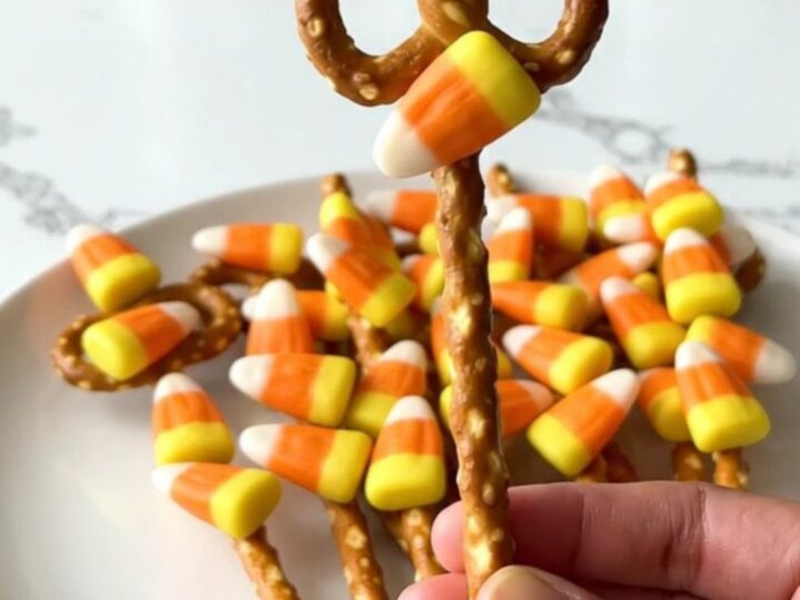 A plate of candy corn pretzel rods featuring a smooth orange candy coating and colorful candy corn pieces.