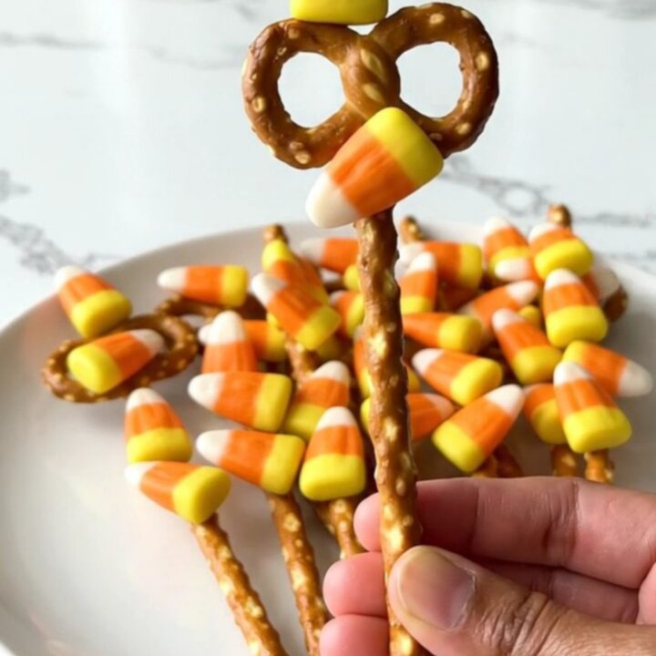 A plate of candy corn pretzel rods featuring a smooth orange candy coating and colorful candy corn pieces.