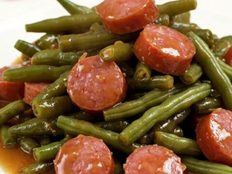 A high-angle shot of a slow cooker filled with smoked sausage coins and fresh green beans in a rich glaze.
