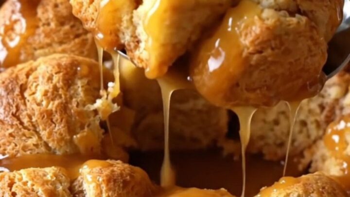 A top-down view of raw biscuit dough pieces in a white dish, being drizzled with amber apple cider caramel sauce.