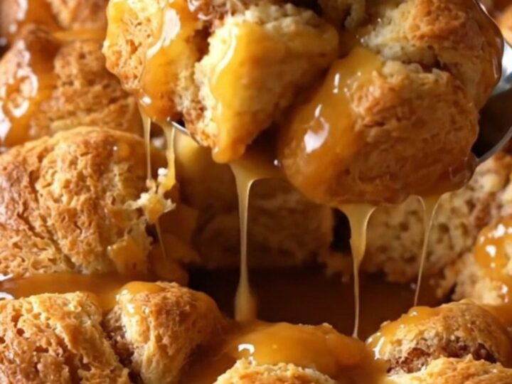 A top-down view of raw biscuit dough pieces in a white dish, being drizzled with amber apple cider caramel sauce.