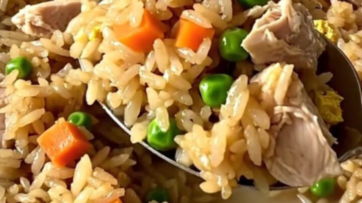 A top-down view of a rectangular baker filled with raw rice, chicken, and colorful vegetables before baking.