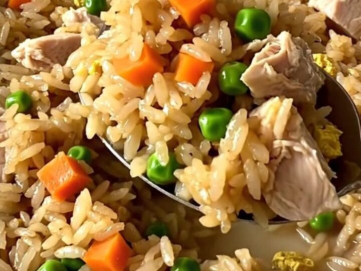 A top-down view of a rectangular baker filled with raw rice, chicken, and colorful vegetables before baking.