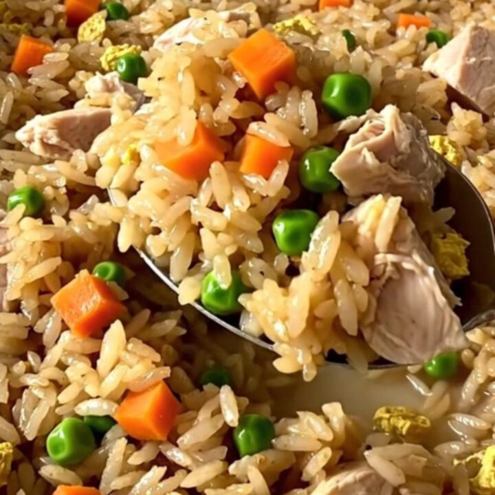 A top-down view of a rectangular baker filled with raw rice, chicken, and colorful vegetables before baking.