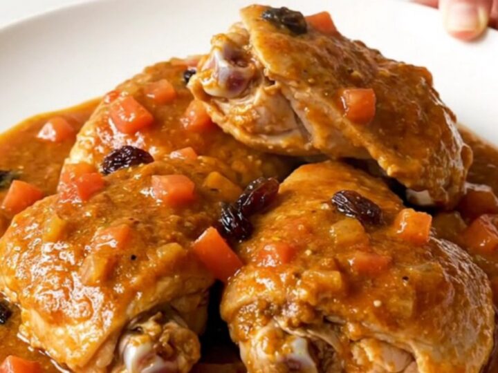 A close-up view of the finished Country Captain chicken served on a white plate with a thick tomato-curry sauce.