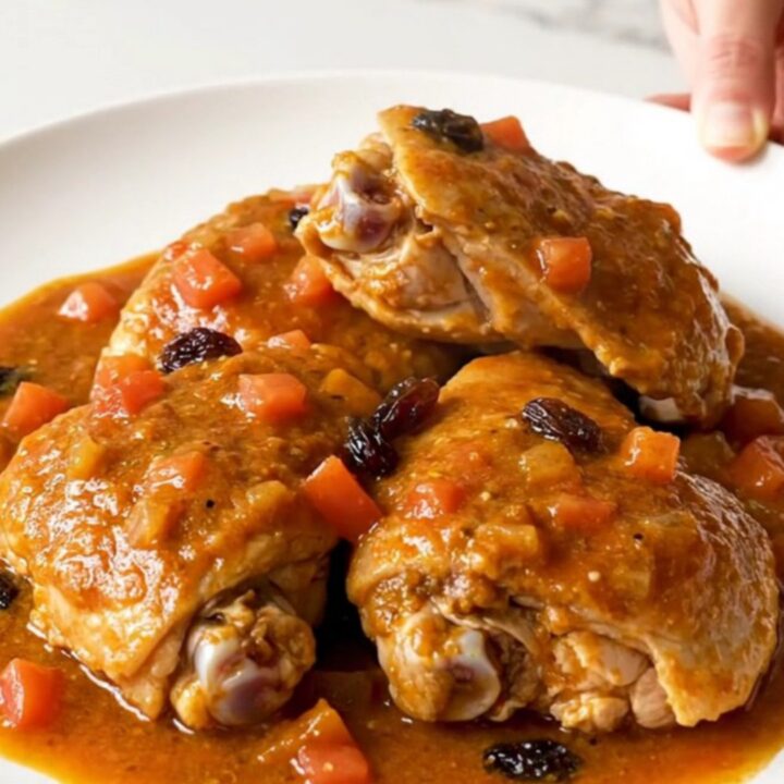 A close-up view of the finished Country Captain chicken served on a white plate with a thick tomato-curry sauce.