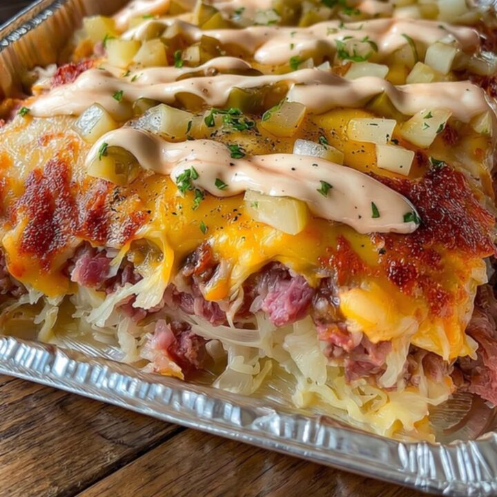 A golden, bubbling Reuben casserole in a foil pan on a wooden countertop.
