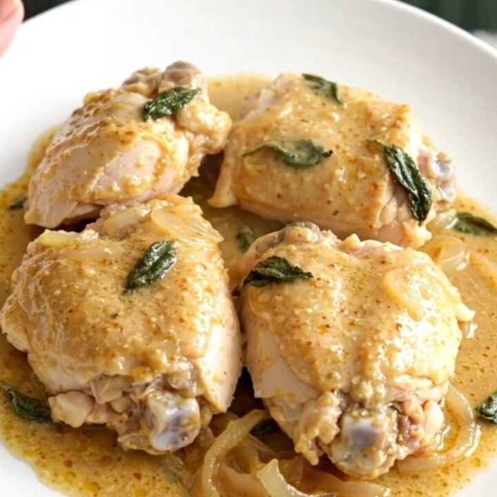 A top-down view of tender chicken thighs in a creamy sage and brown butter sauce inside a slow cooker.