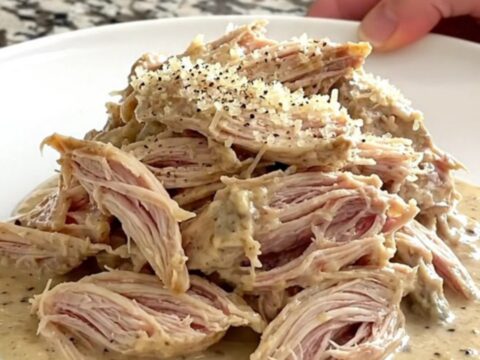 A mound of tender shredded Caesar chicken topped with parmesan cheese in a slow cooker.